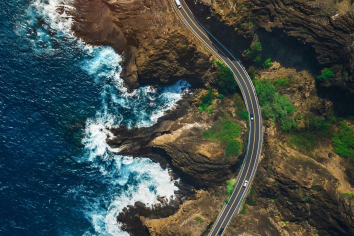 Stunning aerial shot of a winding coastal road in Hawaii with vibrant ocean waves.