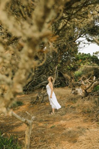 A woman in a white dress stands peacefully in a forest landscape, embracing nature's tranquility.