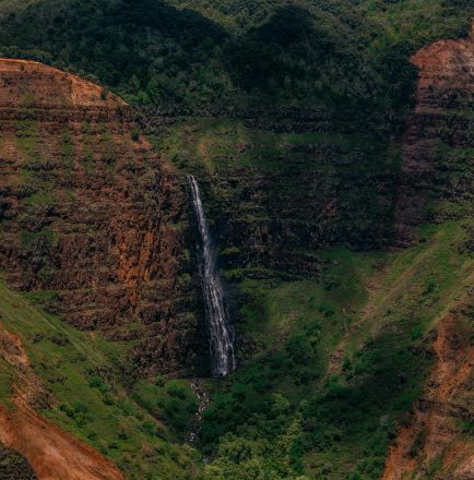 A stunning waterfall cascades down the vibrant cliffs of Waimea Canyon, showcasing diverse geological formations.