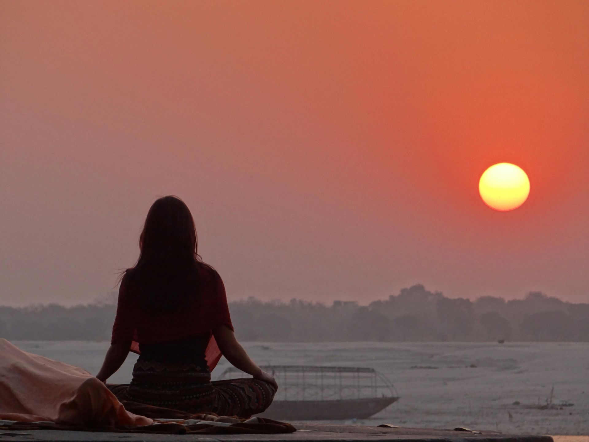 Serene scene of a woman meditating at sunset by the Ganges River in Varanasi, India.