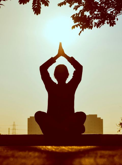 Silhouette of a person practicing yoga outdoors during sunrise, creating a calming atmosphere.