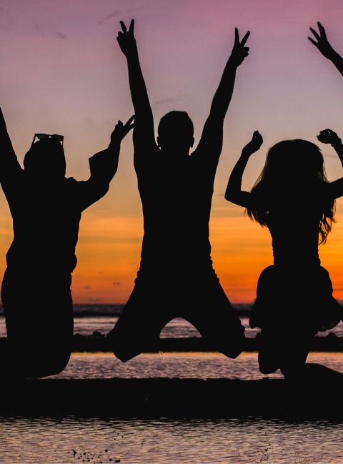 Silhouette of friends jumping on the beach at sunset, celebrating summer fun.